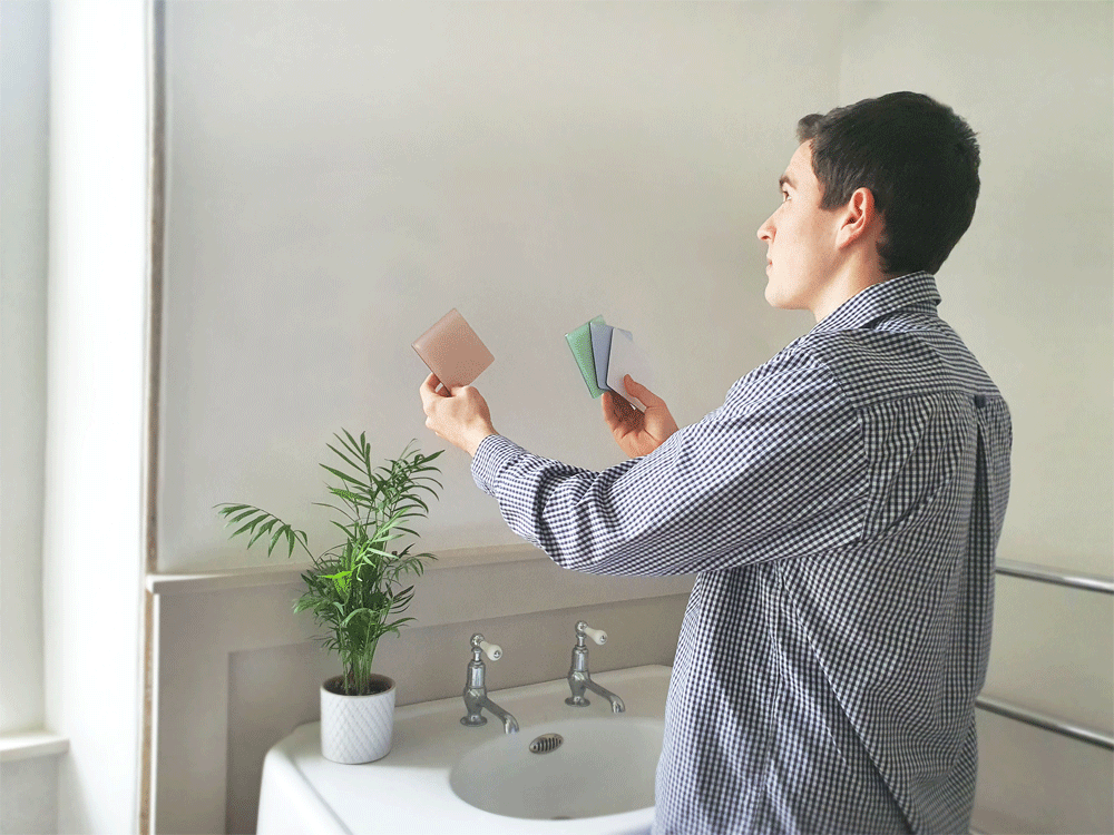 Person comparing coloured splashback samples in a modern bathroom while choosing bespoke acrylic and glass splashback finishes for a home renovation project.